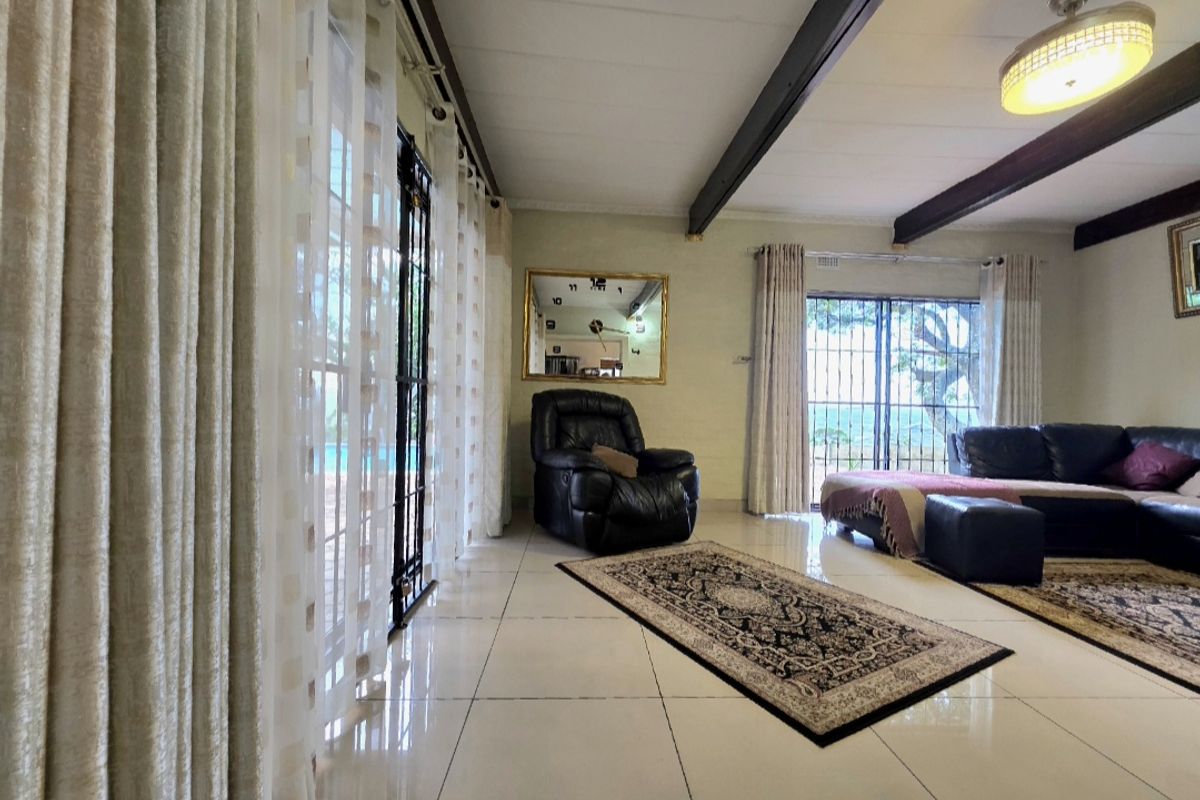 Spacious living room featuring tiled floors, exposed ceiling beams, and large sliding glass doors providing access to the outdoor area.