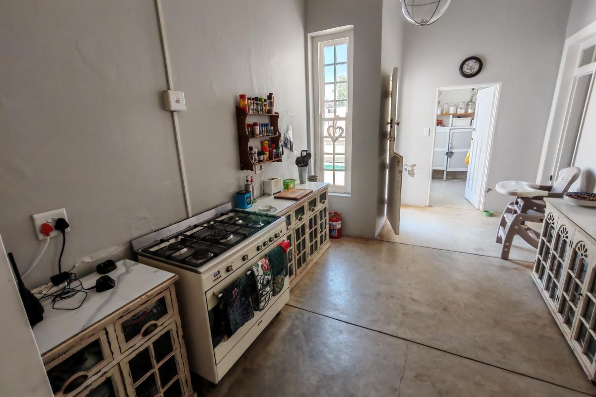 A functional farm-style kitchen featuring a gas stove, built-in cabinetry, and concrete flooring, with an adjacent scullery area visible through the doorway.