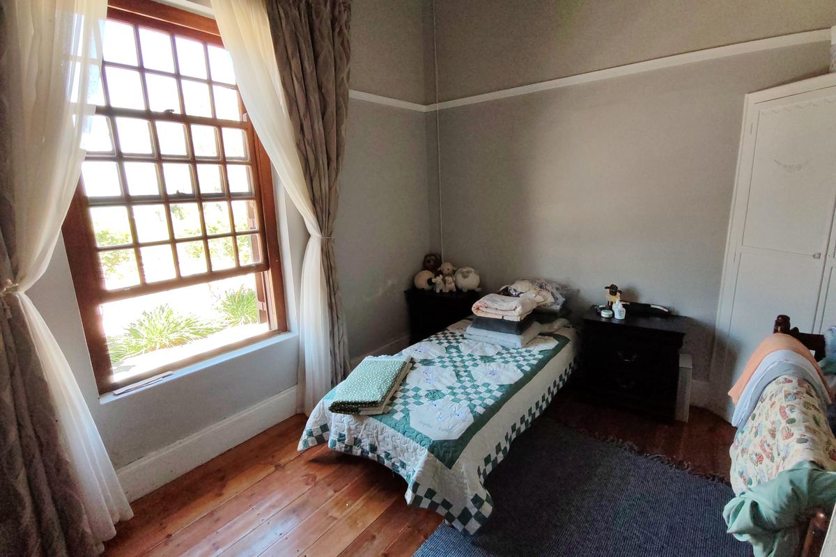 A cozy bedroom featuring original timber flooring, high ceilings with picture rails, and a large multi-pane sash window providing natural light.