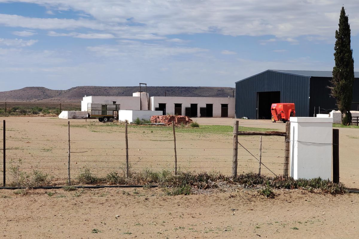 A wide view of the farm property featuring a large metal shed, outbuildings, and open land with wire fencing.