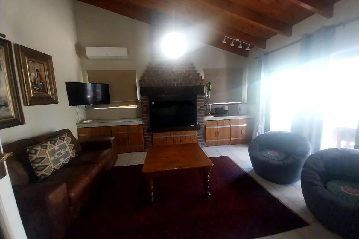 Spacious living room featuring a high vaulted timber ceiling, a prominent brick fireplace, and built-in cabinetry with tiled surfaces.