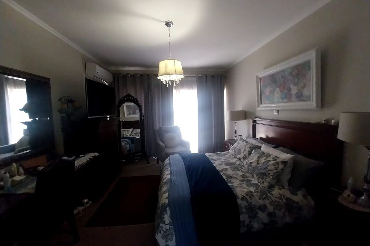 A well-proportioned bedroom featuring a wall-mounted air conditioning unit, neutral wall finishes, and direct access to a window with curtain treatments.