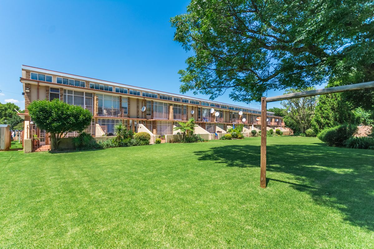 A view of the rear townhouse facade featuring multiple levels with balconies overlooking a large, well-maintained communal garden area.