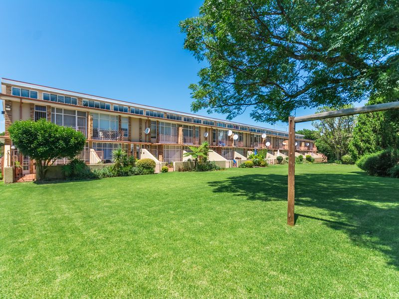 A view of the rear townhouse facade featuring multiple levels with balconies overlooking a large, well-maintained communal garden area.