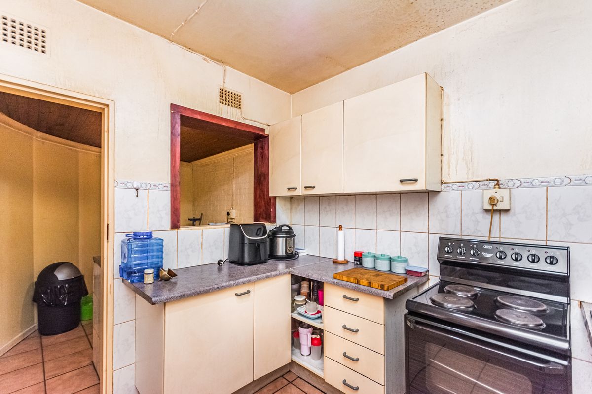 A dated kitchen featuring laminate countertops, built-in cabinetry, and a tiled backsplash, requiring cosmetic updates and repairs to the ceiling and wall finishes.