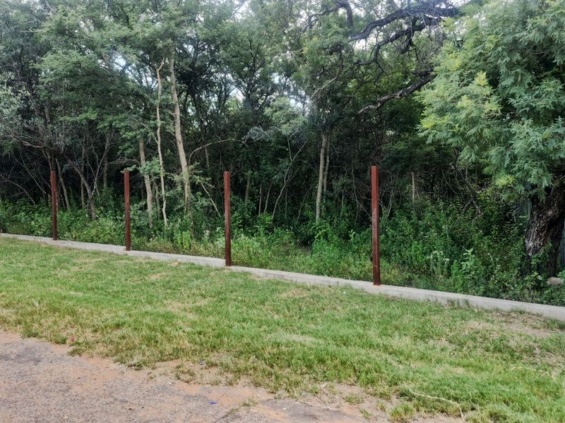 A view of the residential property boundary featuring a concrete base wall with installed metal fence posts, bordering a wooded area.