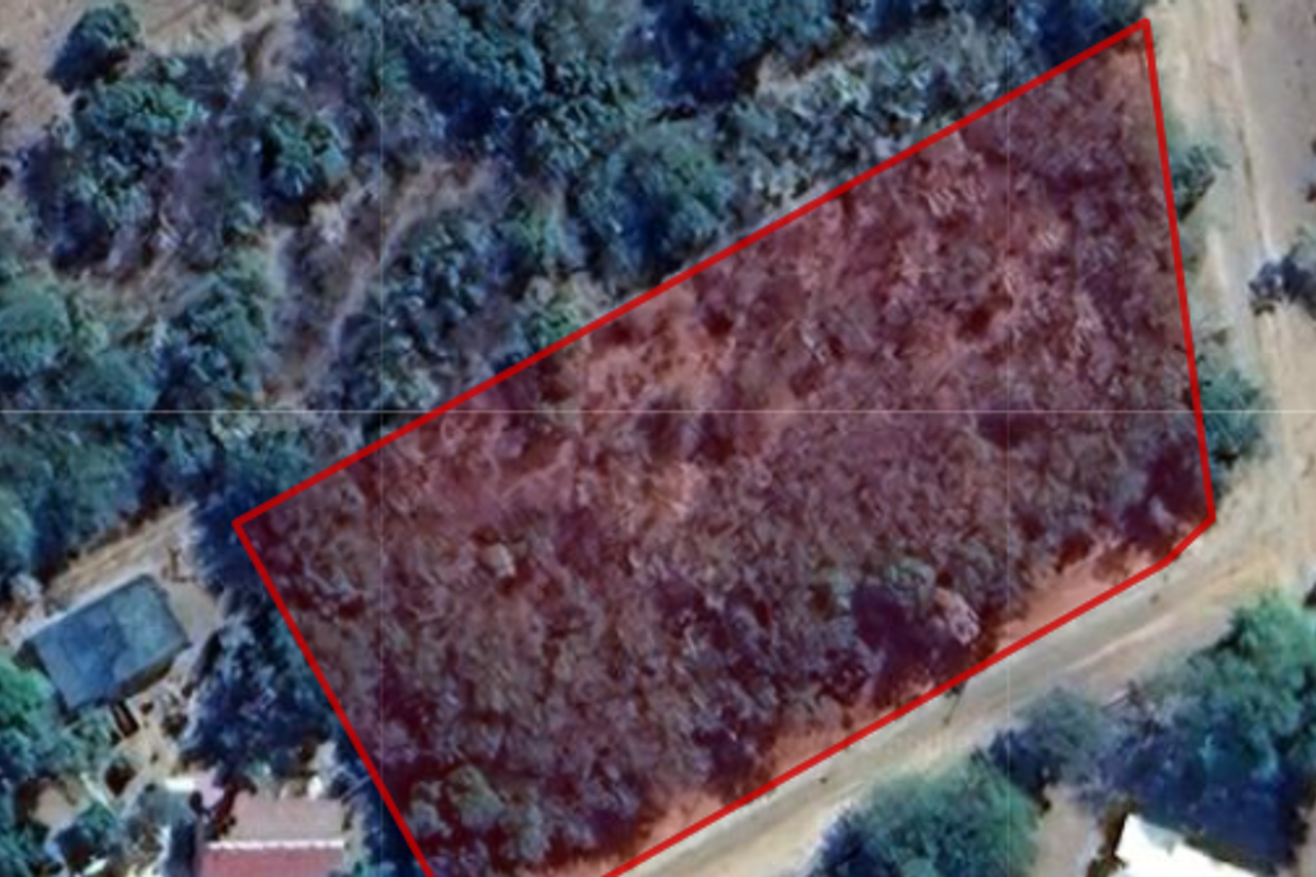 An aerial view of a vacant residential plot outlined in red, featuring natural vegetation and surrounding landscape.