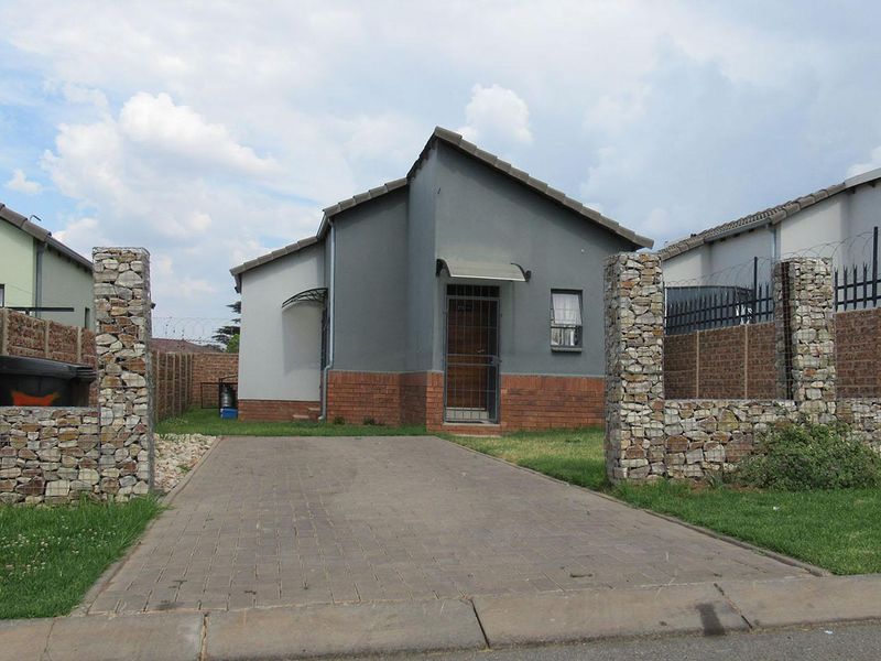 Front view of a detached house featuring a paved driveway, gabion stone entrance pillars, and a secure brick boundary wall.