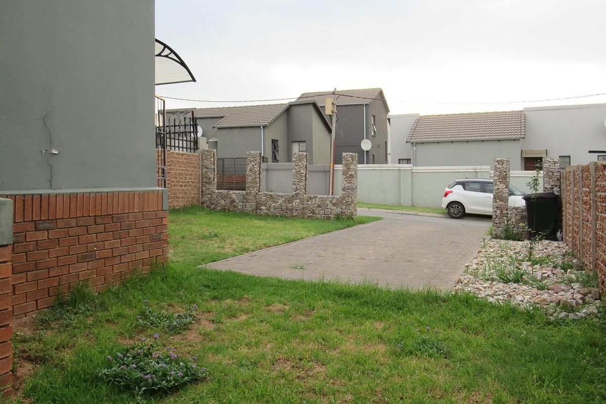 Rear exterior view showing a paved driveway, lawn area, and boundary walling with visible structural cracking on the main building facade.
