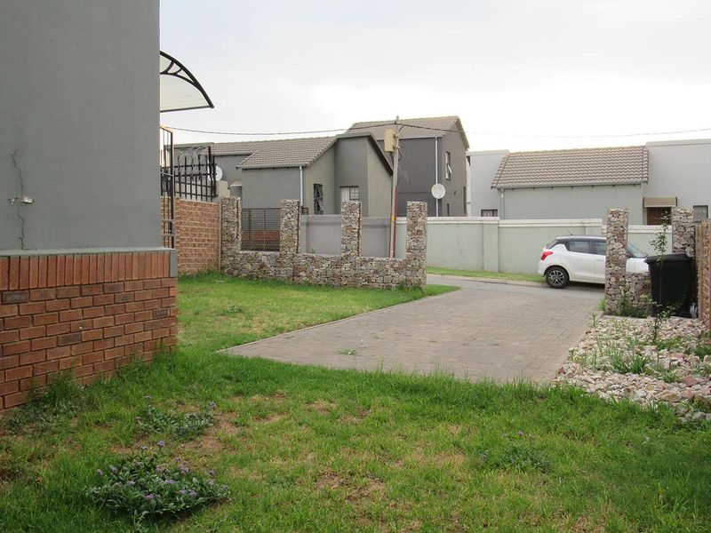 Rear exterior view showing a paved driveway, lawn area, and boundary walling with visible structural cracking on the main building facade.