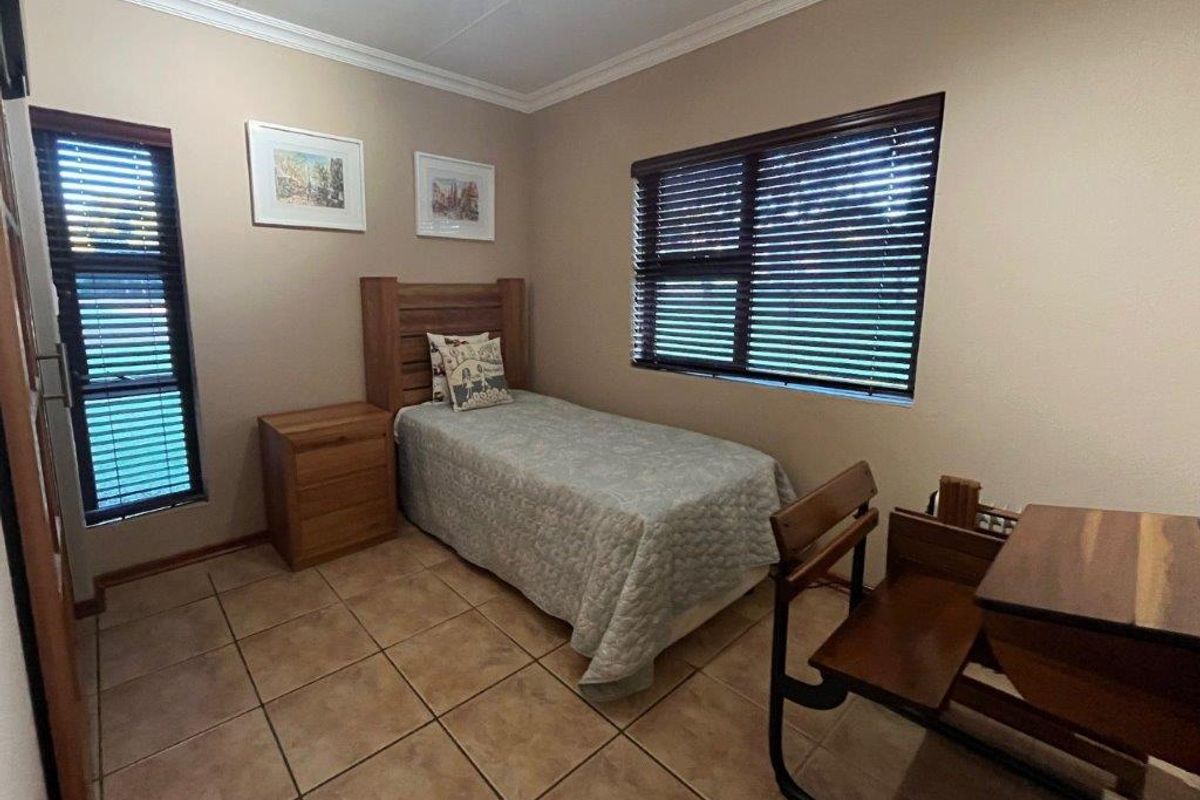A functional bedroom featuring tiled flooring, neutral wall tones, and large windows fitted with dark horizontal blinds.