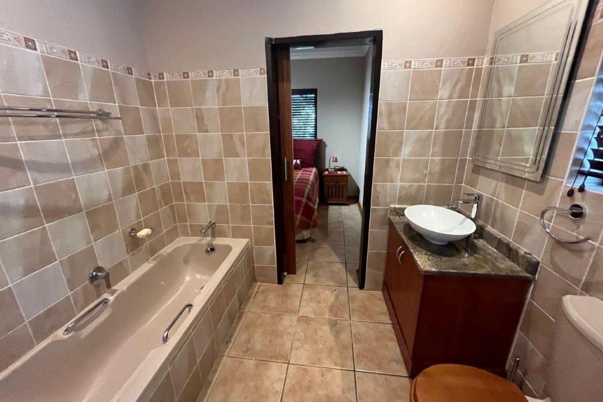 A functional bathroom featuring a built-in bathtub, vanity with vessel sink, and tiled walls, providing direct access to the adjacent bedroom.