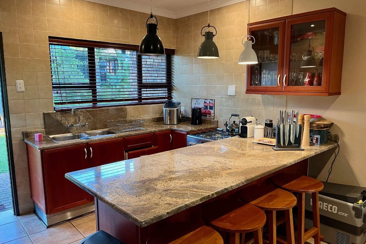 A functional kitchen featuring granite countertops, wooden cabinetry, a gas hob, and a breakfast bar with pendant lighting.