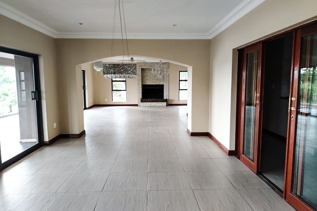 Spacious open-plan living area featuring large format floor tiles, a stone-clad fireplace, and multiple sliding glass doors providing access to the exterior.