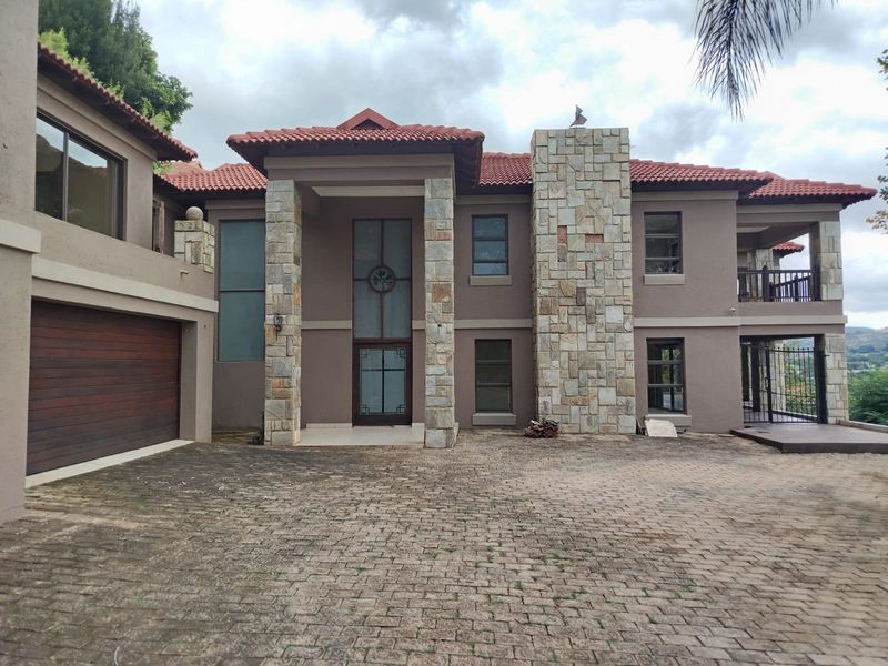 Front elevation of a multi-story residence featuring stone cladding, a tiled roof, and a paved driveway leading to a double garage.