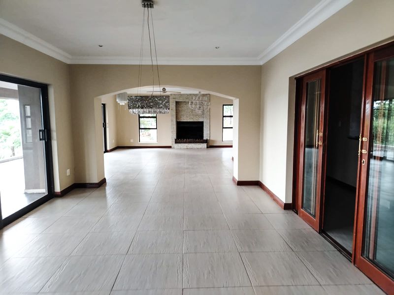 Spacious open-plan living area featuring large format floor tiles, a stone-clad fireplace, and multiple sliding glass doors providing access to the exterior.