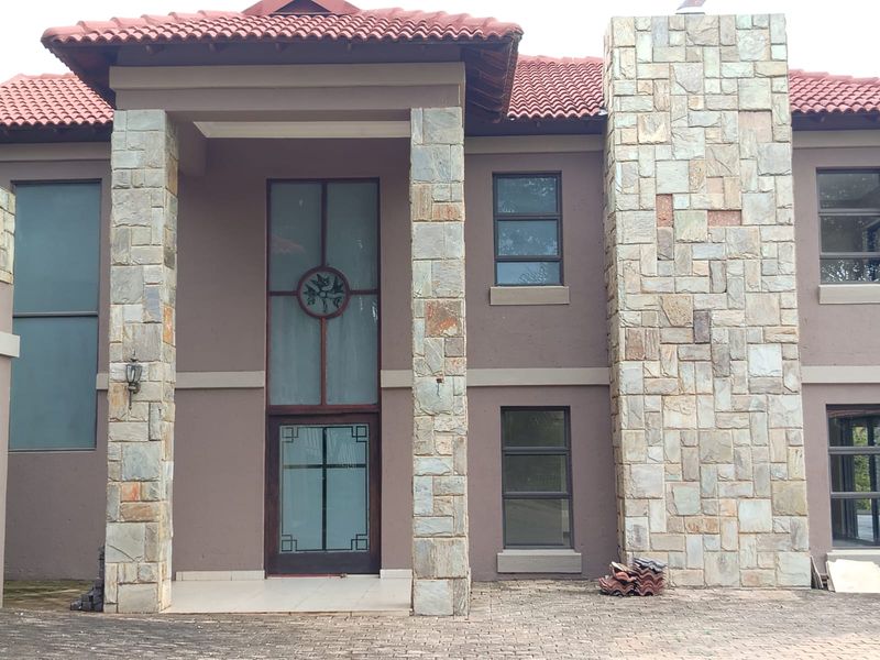 Front elevation of a house featuring stone cladding, terracotta roof tiles, and a large glass entrance door with a paved driveway.