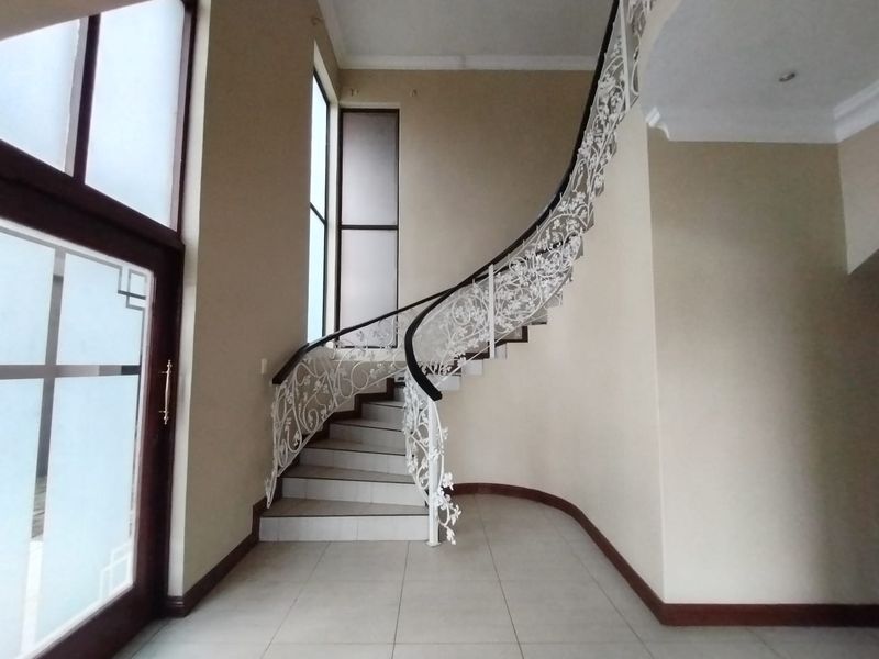 Spacious entrance hall featuring a striking curved staircase with an ornate wrought iron balustrade and neutral tiled flooring.