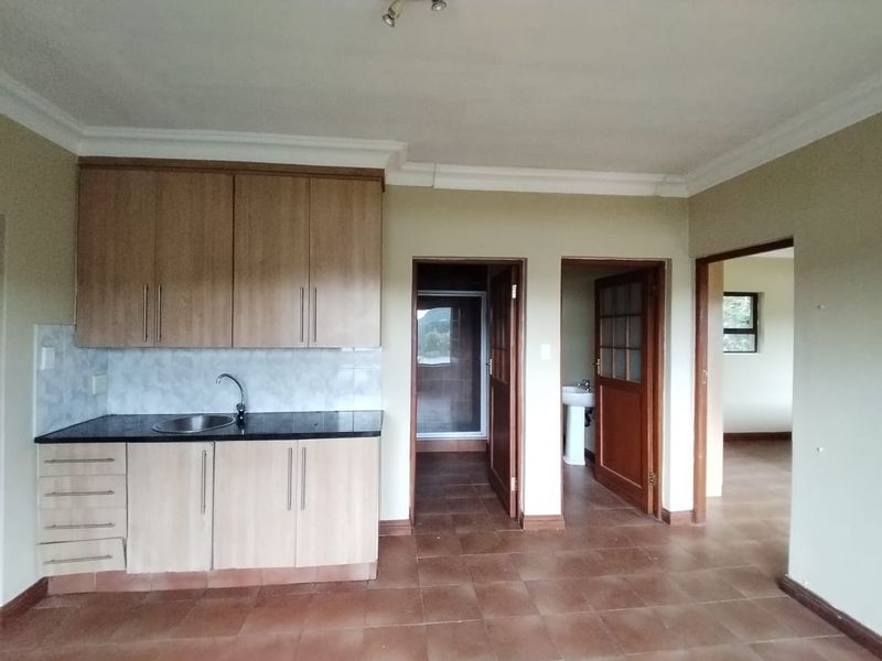 A functional kitchen area featuring built-in cabinetry, laminate countertops, and tiled flooring, with direct access to adjacent rooms.