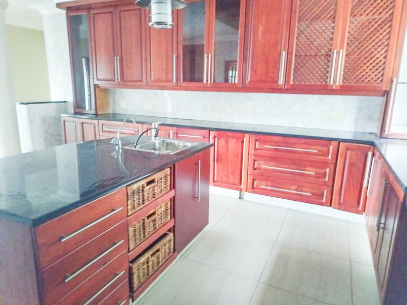 Spacious kitchen featuring extensive wooden cabinetry, a large central island with granite countertops, and tiled flooring throughout.