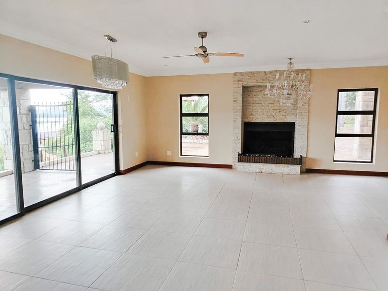 Spacious living room featuring a stone-clad fireplace, large sliding glass doors leading to a patio, and neutral tiled flooring.
