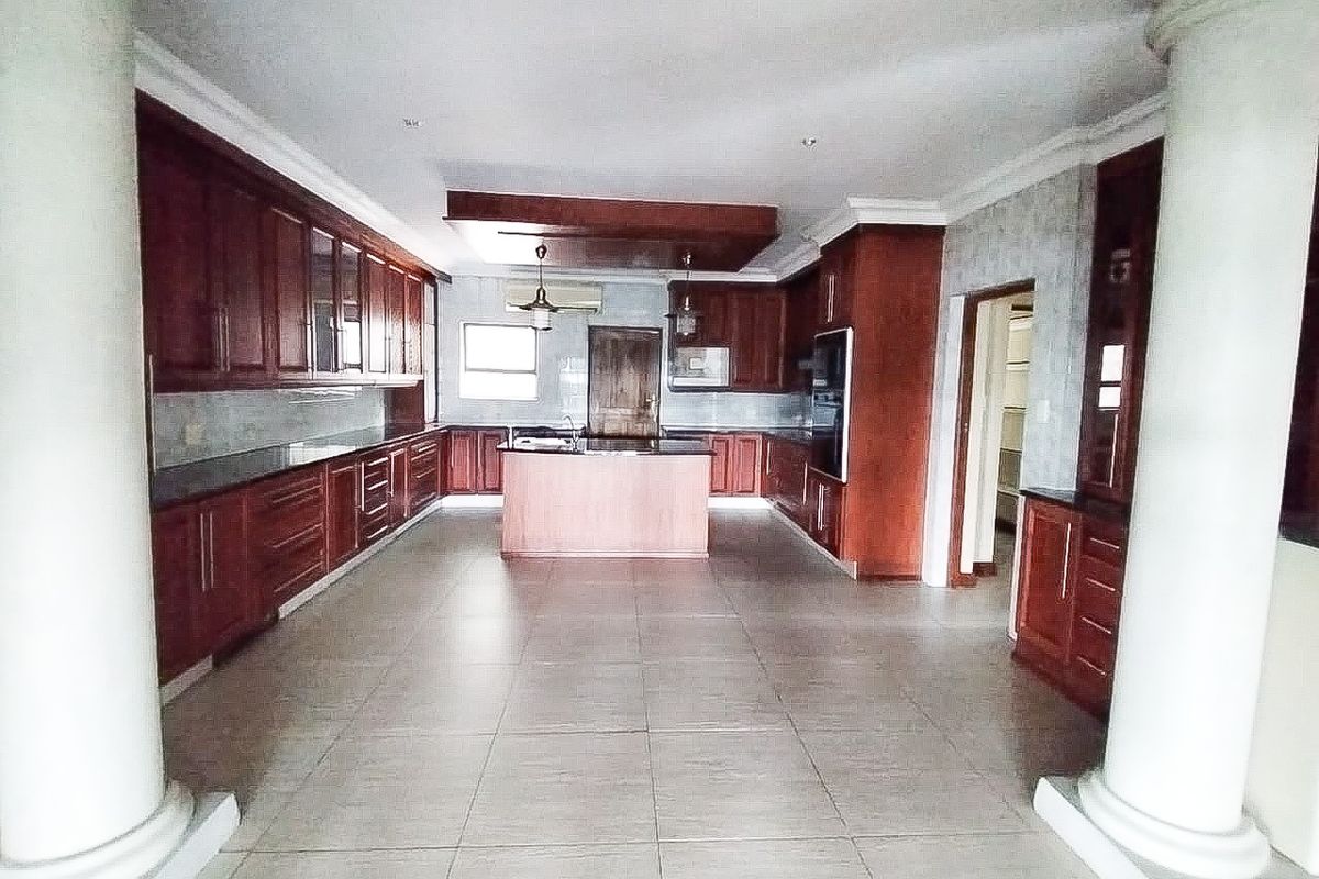 Spacious kitchen featuring extensive wooden cabinetry, granite countertops, a central island, and tiled flooring, framed by decorative architectural columns.