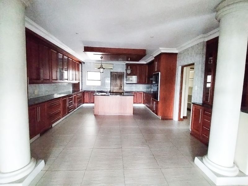Spacious kitchen featuring extensive wooden cabinetry, granite countertops, a central island, and tiled flooring, framed by decorative architectural columns.