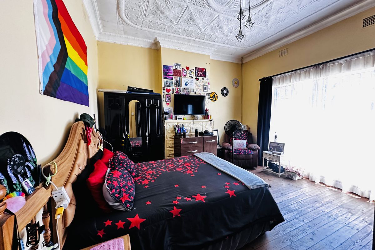 Spacious bedroom featuring original ornate plaster ceilings, a decorative fireplace mantel, and classic timber floorboards, offering a character-filled space with abundant natural light.