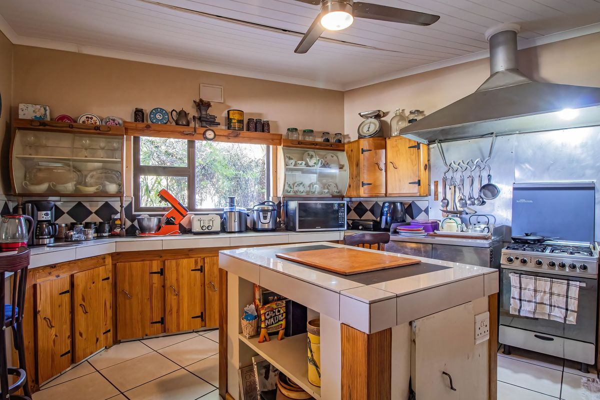 A functional kitchen featuring wooden cabinetry, tiled countertops, a central island, and a stainless steel extractor fan over a gas hob.