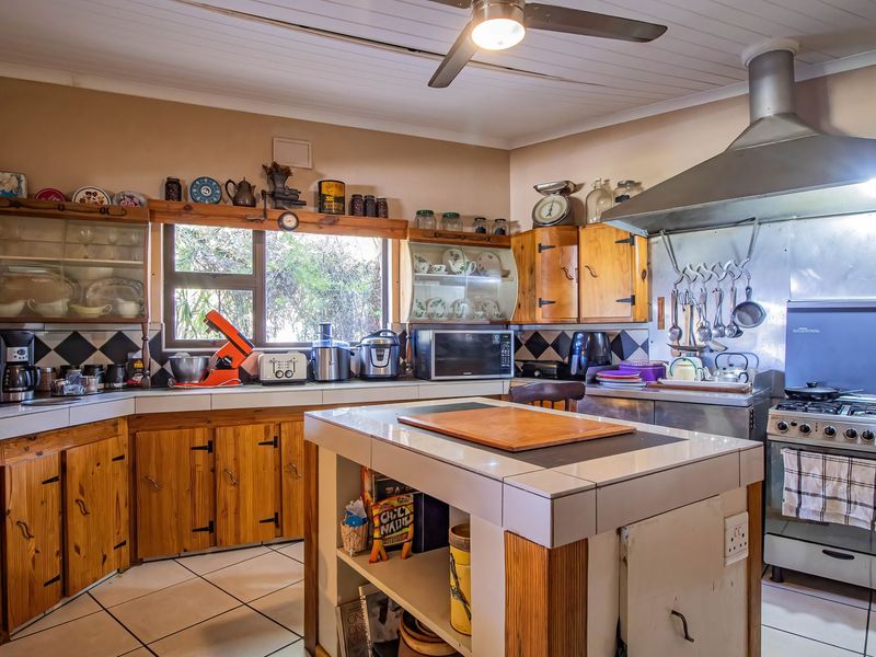 A functional kitchen featuring wooden cabinetry, tiled countertops, a central island, and a stainless steel extractor fan over a gas hob.