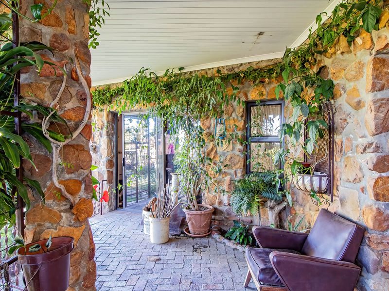 A charming covered patio featuring rustic stone walls, brick paving, and a beadboard ceiling, providing a cozy outdoor living space.