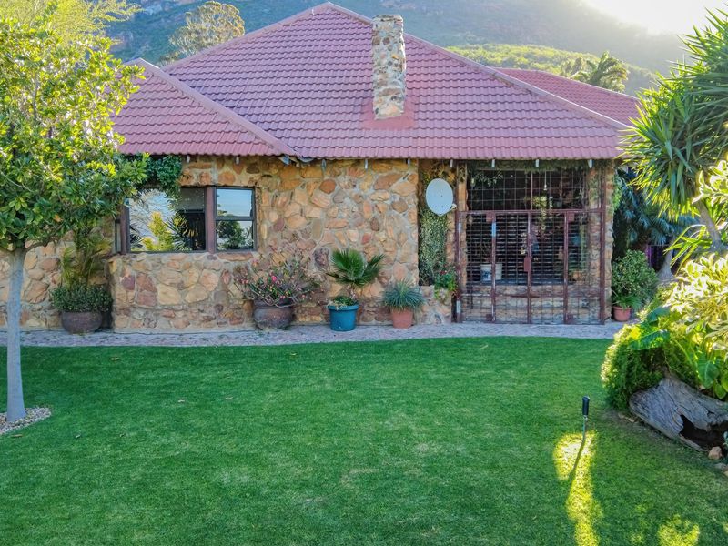 Rear view of a stone-clad house featuring a tiled roof, stone chimney, and a well-maintained lawn with a paved walkway.