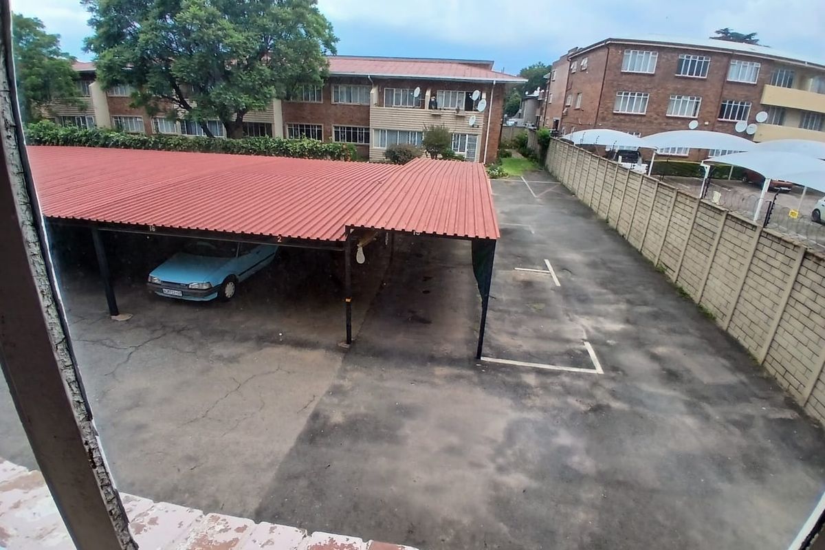 Elevated view of the complex parking area featuring a covered carport structure and paved driveway with boundary walling.