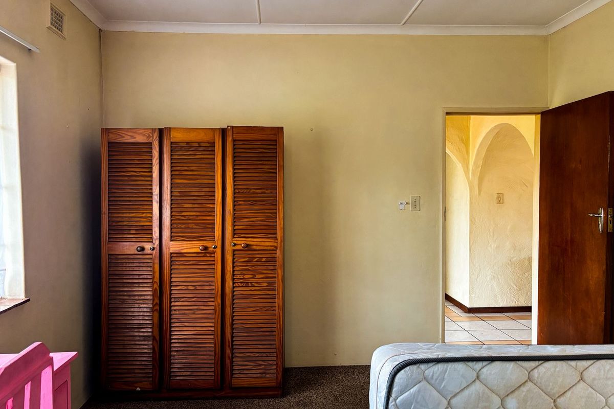 A bedroom featuring carpeted flooring, coved ceilings, and a view through an archway into the adjacent living space.