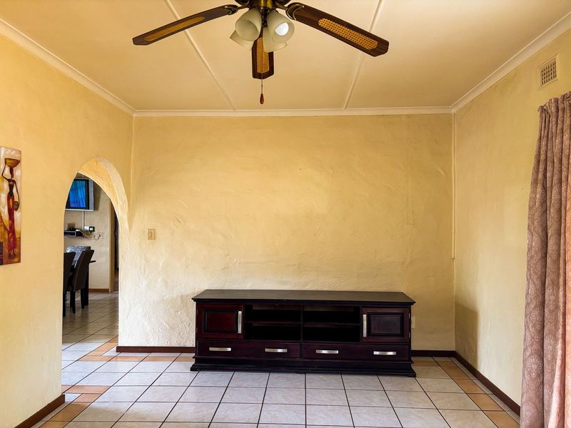 A living room featuring ceramic floor tiles, a ceiling fan, and an arched doorway leading to an adjacent space.