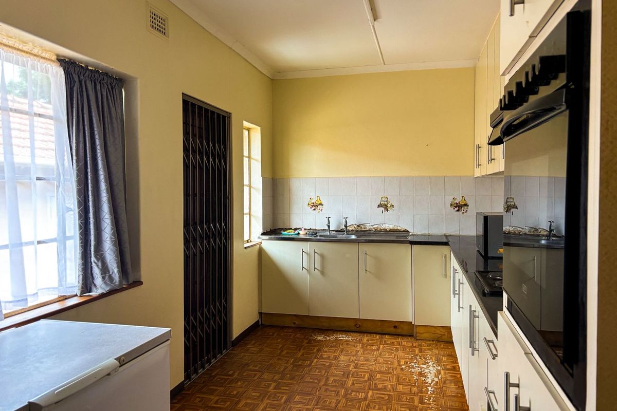 A dated kitchen featuring built-in cabinetry, a stainless steel sink, and a built-in oven, currently showing signs of wear and water damage on the floor.