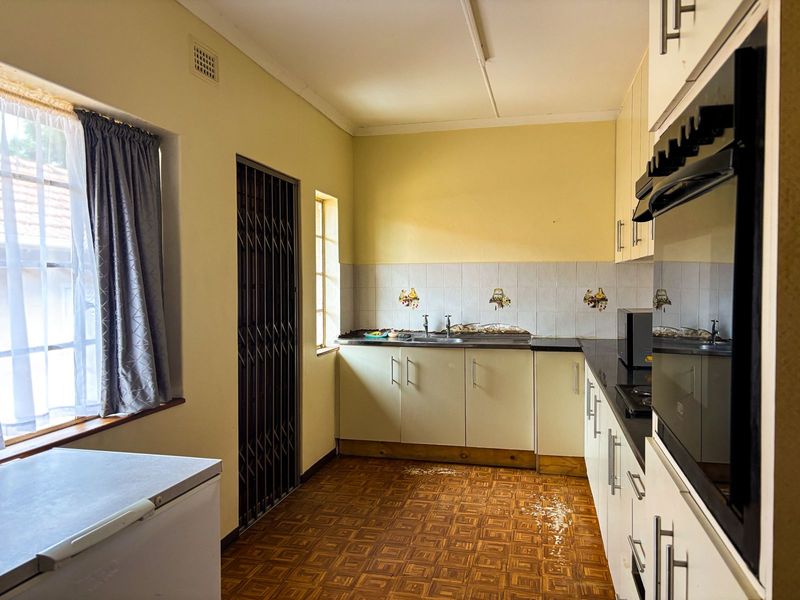 A dated kitchen featuring built-in cabinetry, a stainless steel sink, and a built-in oven, currently showing signs of wear and water damage on the floor.