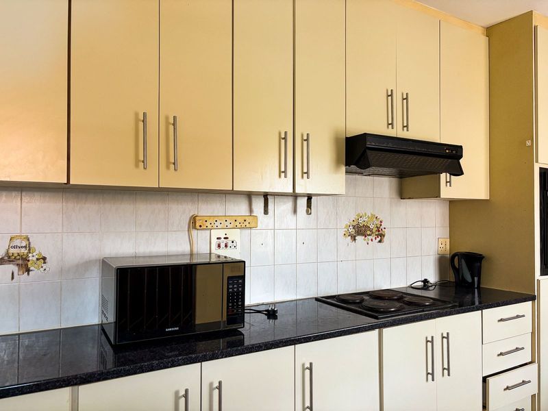A functional kitchen featuring built-in cabinetry, dark laminate countertops, an electric hob, and an extractor fan with a tiled backsplash.