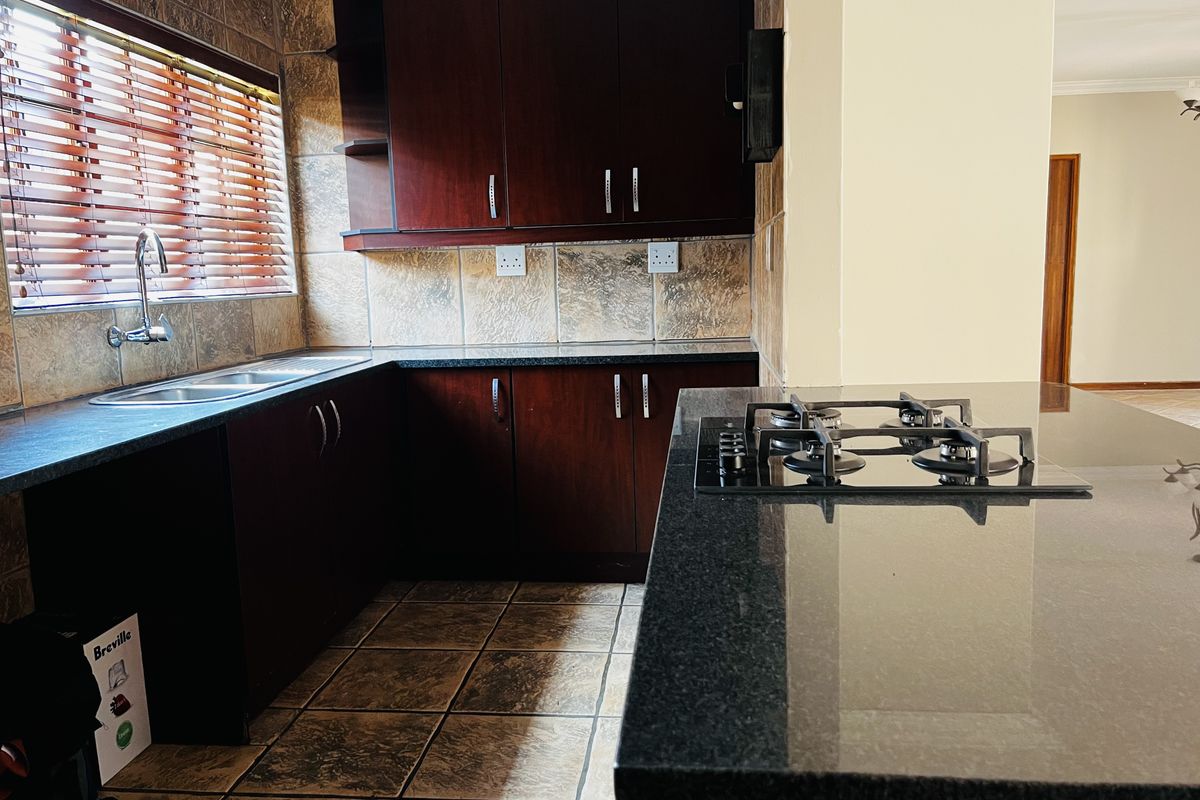 A functional kitchen featuring dark wood cabinetry, granite countertops, a built-in gas hob, and tiled splashbacks with a double sink.