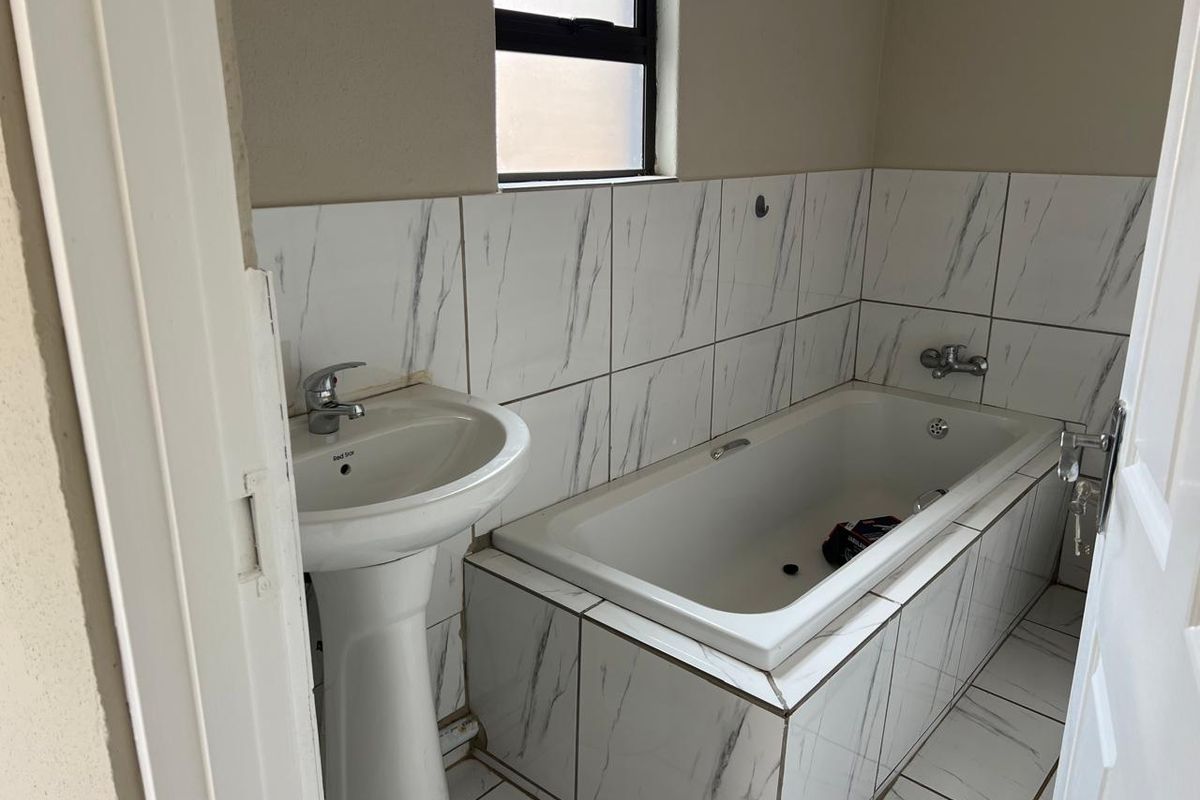 A compact bathroom featuring a pedestal basin, a built-in bathtub with marble-look wall tiling, and tiled flooring.
