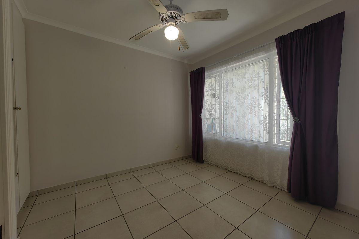 A bright, empty bedroom featuring neutral tiled flooring, a ceiling fan, and a built-in cupboard, offering a clean canvas for personalization.