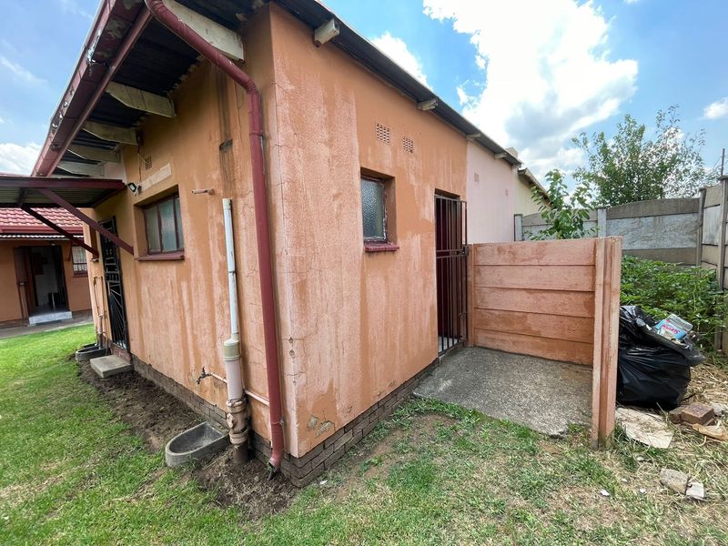 Rear exterior view of the property showing weathered plaster walls, a concrete apron, and security gate access.