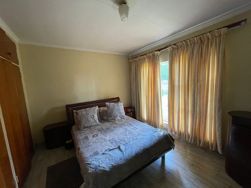 A functional bedroom featuring tiled flooring, built-in cupboards, and natural light through large windows with curtains.