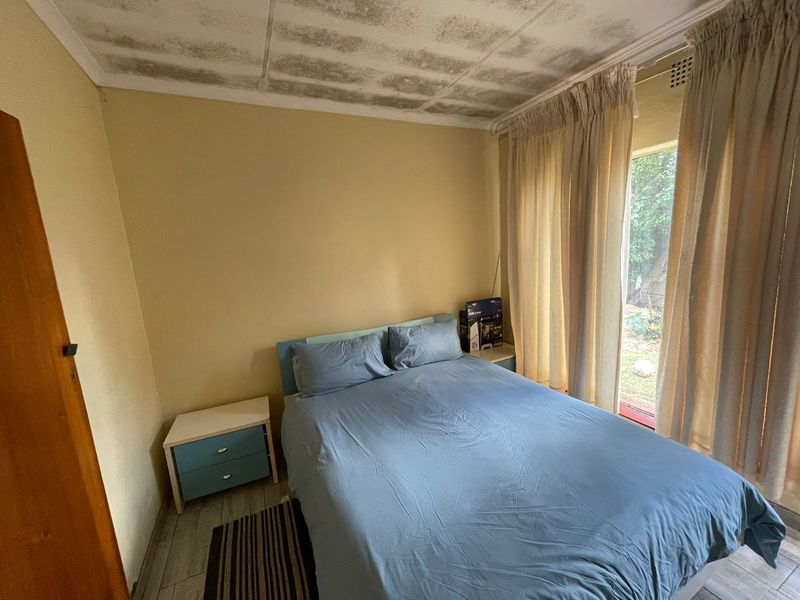 A bedroom featuring tiled flooring and a sliding glass door providing natural light. The ceiling shows signs of water staining and requires maintenance.