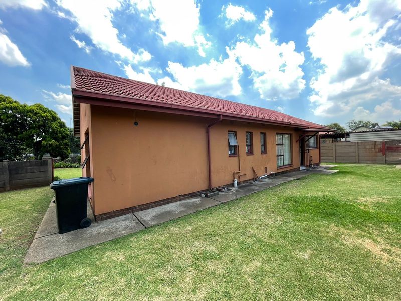 Rear exterior view of the house featuring a tiled roof, concrete apron, and surrounding garden area with perimeter walling.