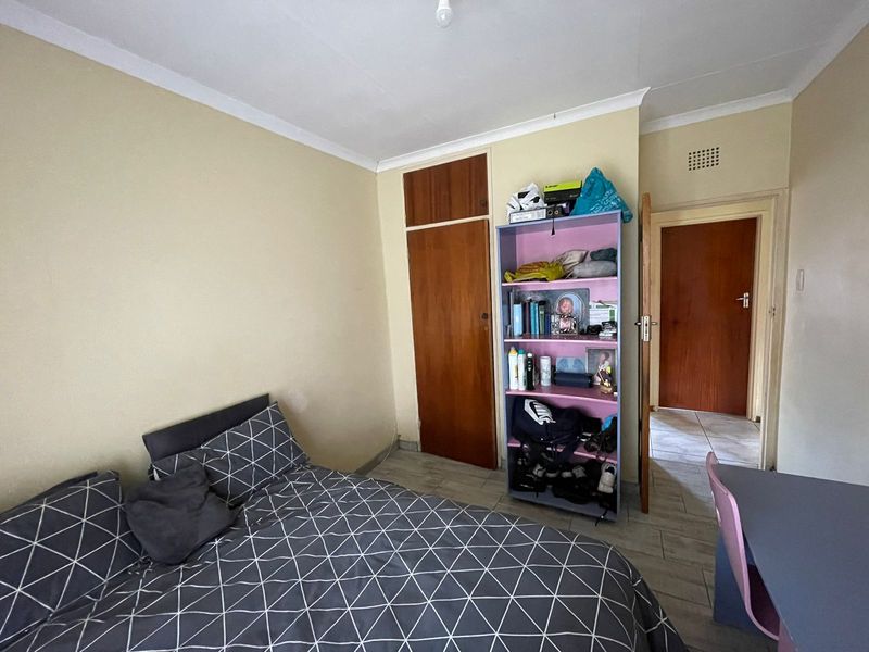 A functional bedroom featuring tiled flooring, a built-in cupboard, and neutral wall finishes, providing a practical space for rest.