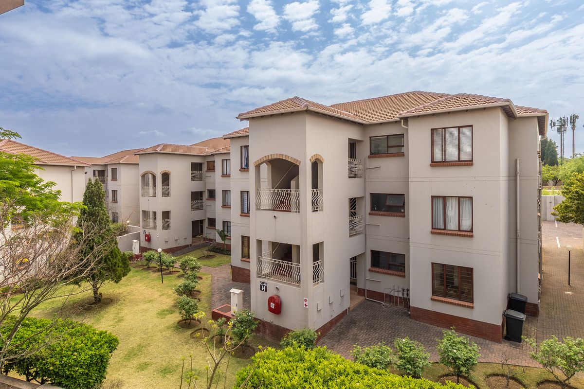 Exterior view of a multi-story apartment complex featuring tiled roofing, paved walkways, and landscaped garden areas.