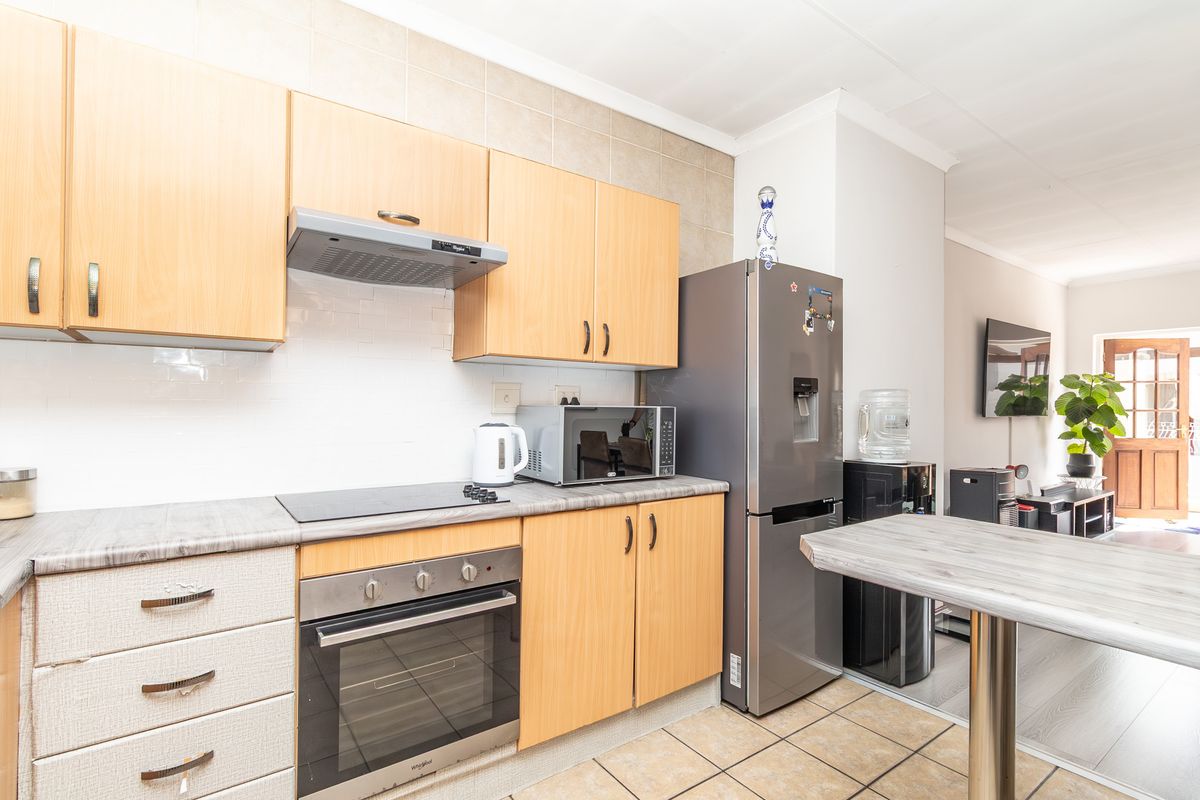 A functional kitchen featuring light wood cabinetry, a built-in oven, hob, and extractor fan, with tiled flooring and a breakfast bar area.