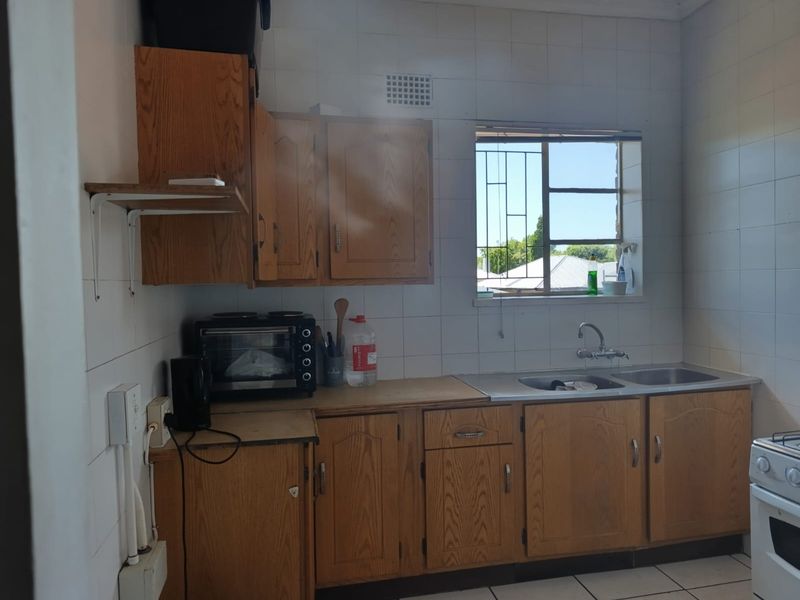 A functional kitchen featuring wooden cabinetry, a double stainless steel sink, tiled splashbacks, and security bars on the window.