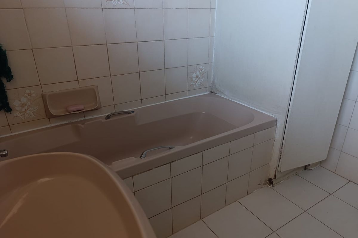 A dated bathroom featuring a built-in bathtub with ceramic wall and floor tiling, requiring cosmetic updates to modernize the space.